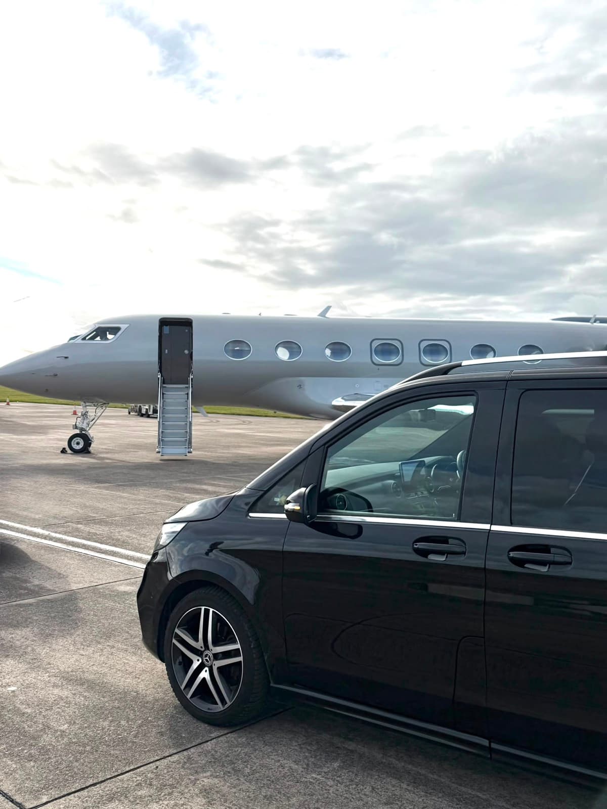 MGM Travels chauffeur opening the rear door of a Mercedes executive car at an airport terminal